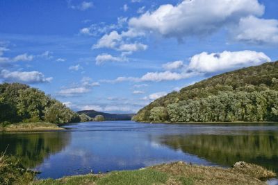 A serene lake surrounded by green hills under a blue sky.
