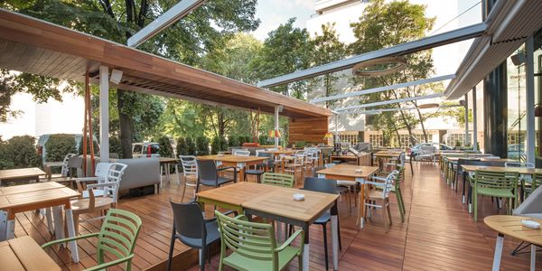 Spacious outdoor restaurant seating with wooden flooring and greenery.