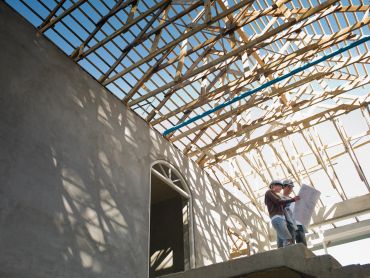 Two construction workers reviewing plans inside a building framework.