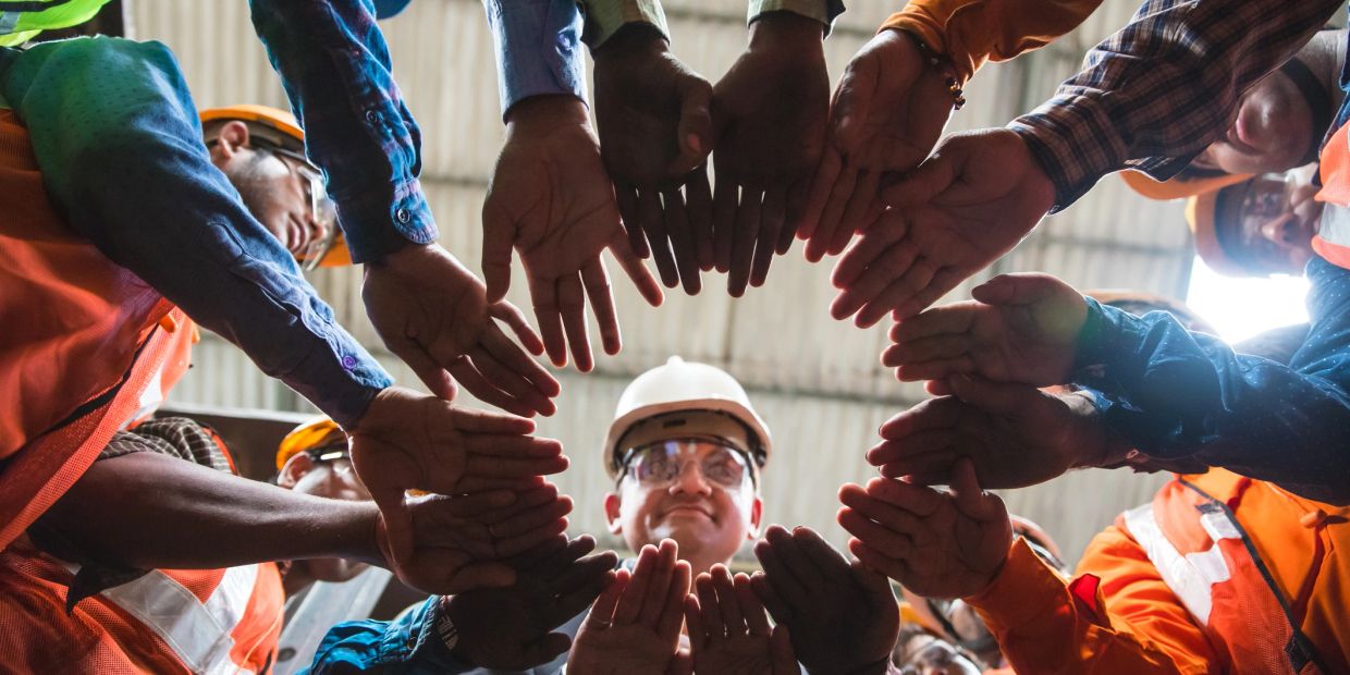 Construction workers forming a circle with hands open in the center.