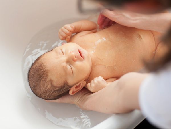 Newborn baby peacefully bathing with gentle support from an adult's hands.