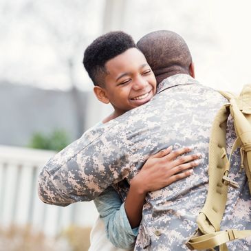 A boy hugging a soldier joyfully.