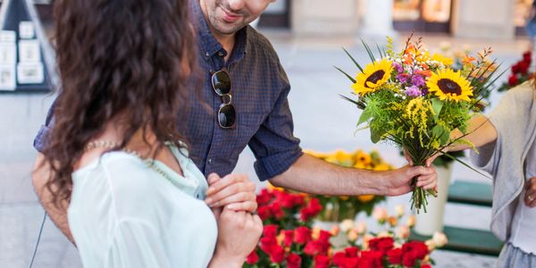 Man giving a bouquet of flowers to a woman at an outdoor market.