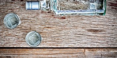 Bottle of alcohol and two shot glasses on wooden surface.