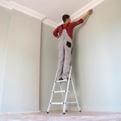 Man painting ceiling trim from ladder.