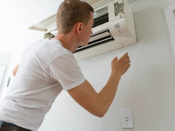 A man inspects a wall-mounted air conditioner indoors.