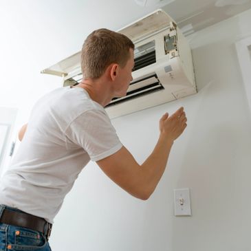 Man inspecting a wall-mounted air conditioning unit indoors.