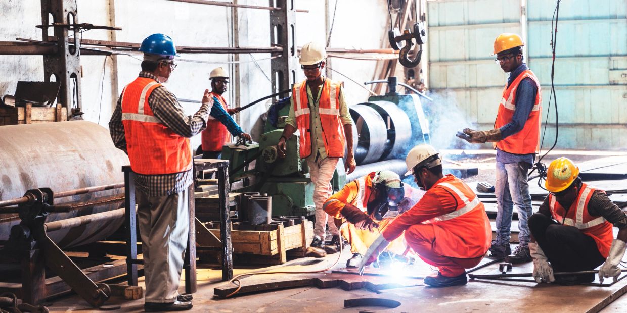 Workers welding and handling machinery in a factory.