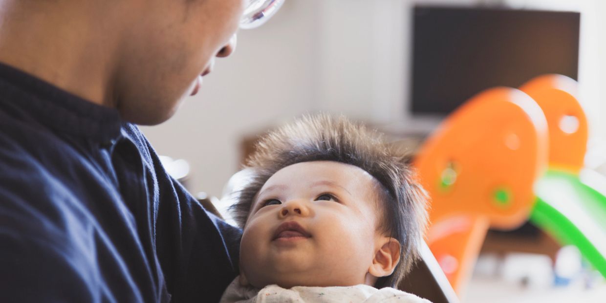 A baby looks up at an adult holding them in a cozy room.