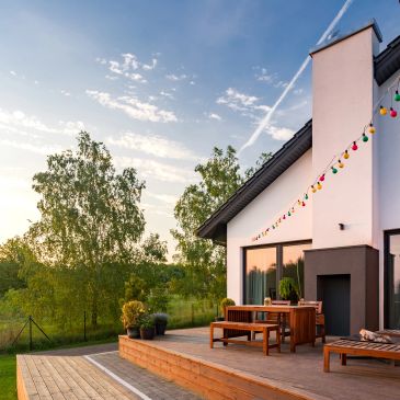 Modern house patio with wooden furniture and colorful lights.