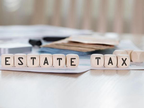 Wooden blocks spelling 'ESTATE TAX' on a table with documents and coins.