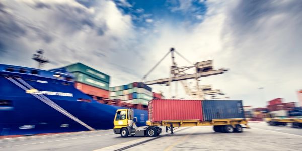 Truck carrying shipping containers at a busy port.