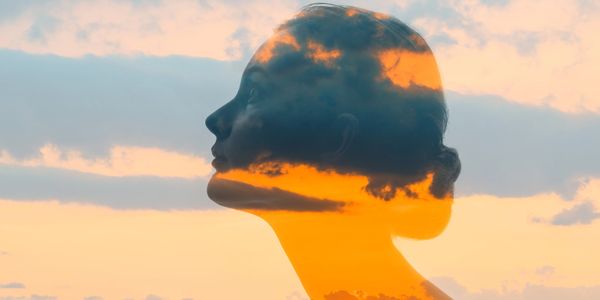 Double exposure of a woman's profile and a vibrant sunset over a cityscape.
