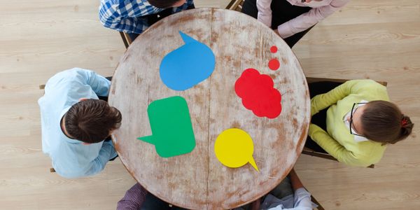Five people sit around a round table with colorful speech bubble cutouts.