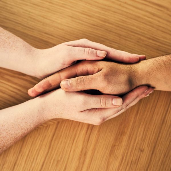 Two hands of different skin tones gently holding each other on a wooden surface.