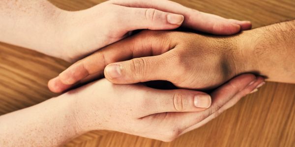 Two pairs of hands gently holding each other on a wooden surface.