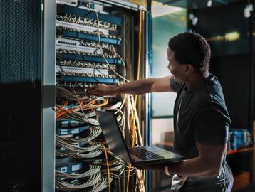 Technician working on server rack with laptop in a data center.