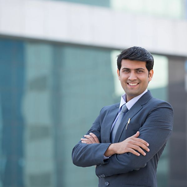 Confident businessman smiling with arms crossed outside a modern office building.