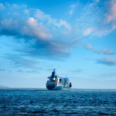 A cargo ship loaded with containers sailing on the ocean under a blue sky.