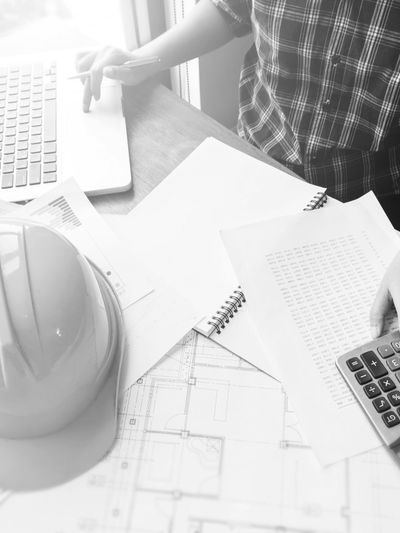 Engineer calculating project costs with a calculator and laptop.