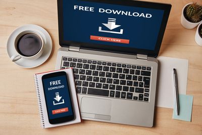 Laptop and smartphone showing free download prompts on a wooden desk.