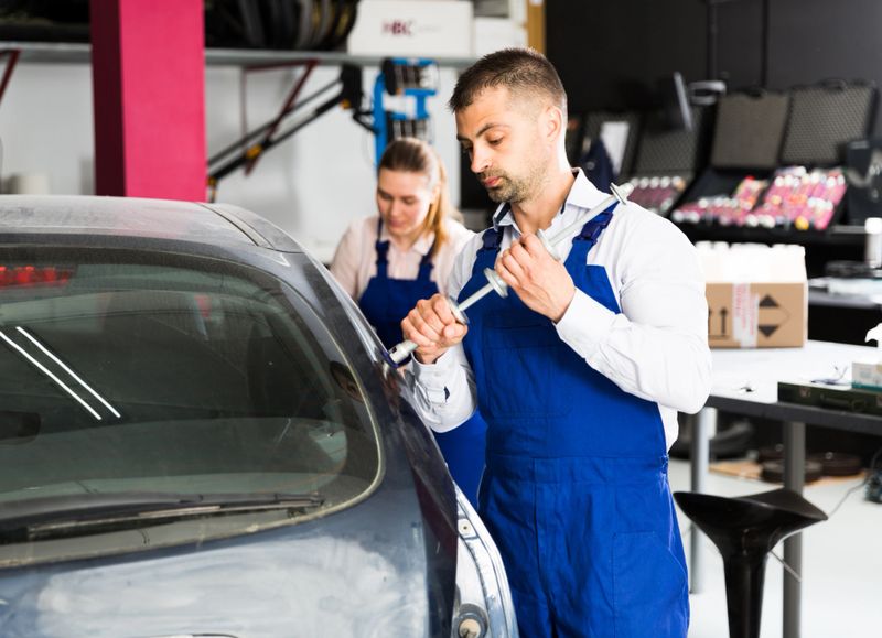 Professional mechanic performing dent repair on car body before painting in auto workshop