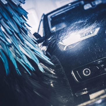 Black car undergoing a wash with water and brushes.