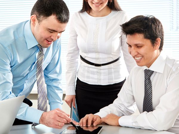 Three professionals collaborating over a tablet in an office.