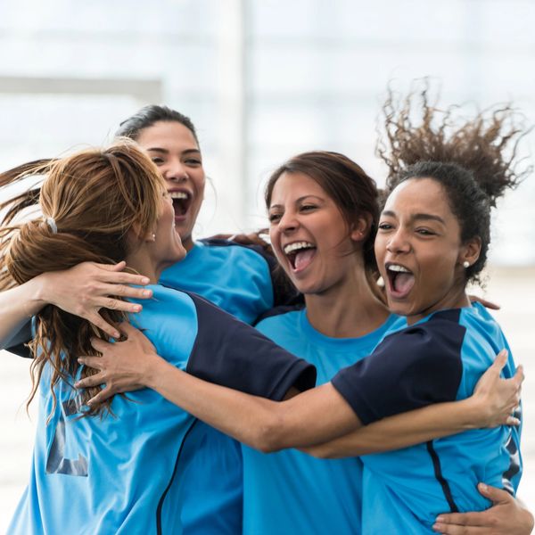Female sports team celebrating joyfully with a group hug.