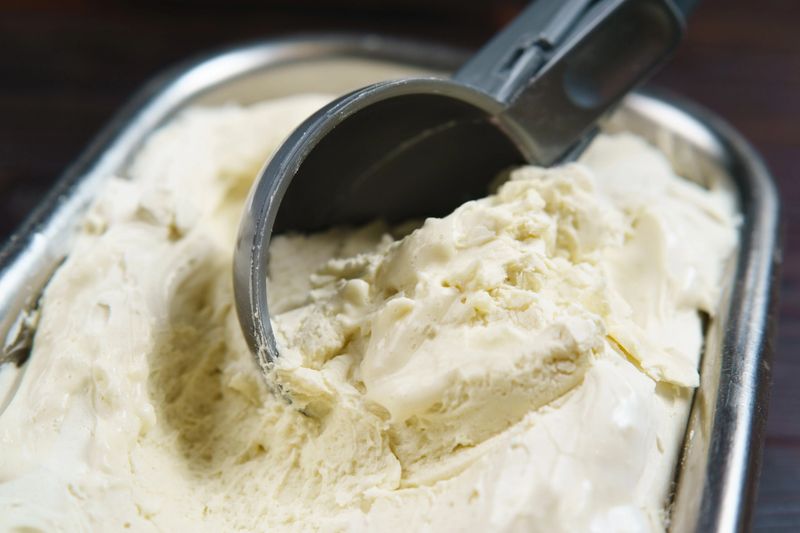 Vanilla ice cream scooped from container with spoon, close up. Food background, ice cream store, traditional seasonal refreshing handmade cold sweets