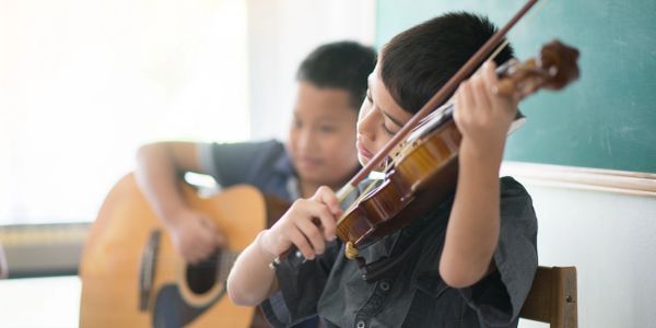 Two boys playing musical instruments, one violin and one guitar.