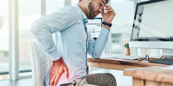 Man experiencing lower back pain while working at a desk, highlighting the importance of ergonomic seating and posture support.