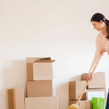 A woman sweeps the floor in a room with moving boxes.