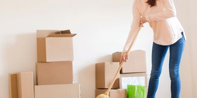 A woman sweeps the floor in a room with moving boxes.