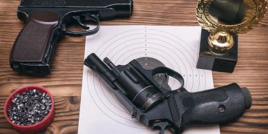Two guns with a target and trophy on a table.