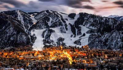 A mountain town illuminated at dusk with snowy slopes in the background.