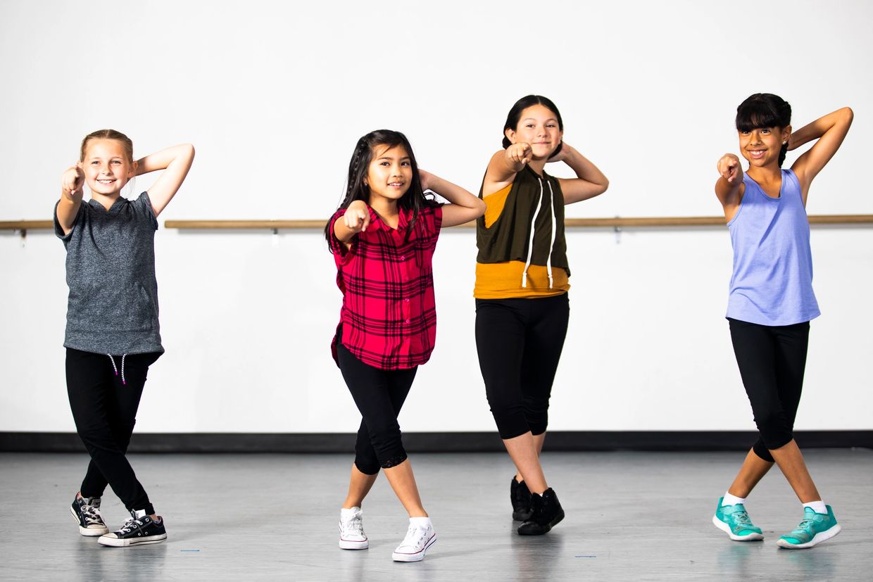 Four girls in casual clothes striking a confident dance pose in a studio.