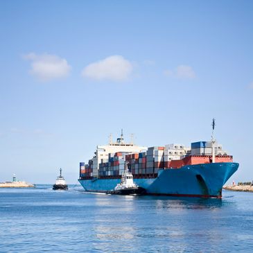 Large cargo ship guided by tugboats in a harbor under a clear sky.