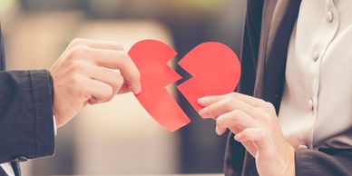 Two people each hold half of a broken red heart symbolizing a breakup.