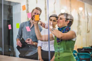 Three colleagues brainstorming ideas using sticky notes on a glass wall.