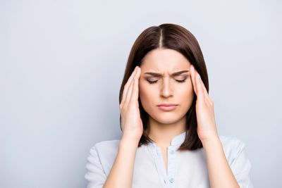 A woman experiencing a headache, touching the sides of her head.