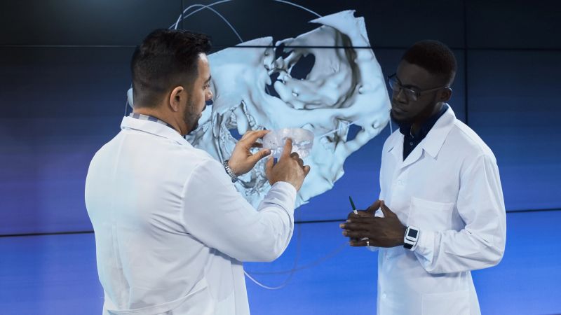 Diverse professional scientists in medical robes having 3-D printed model of human cranium exploring its peculiarities.