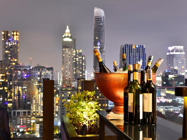 Bottles of wine and champagne on a rooftop bar with city skyline at night.