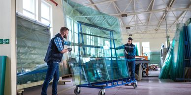 Two workers carefully handling large glass panels inside a factory.
