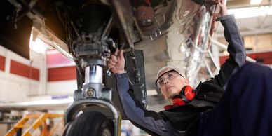 Technician inspecting and repairing an aircraft's landing gear in a hangar.