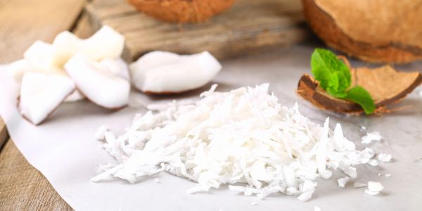Freshly grated coconut with coconut pieces and shells on a wooden surface.