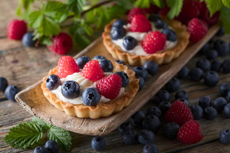Dessert tarts with raspberries and blueberries on a wooden table. Closeup of fancy gourmet fresh berry dessert tarts.