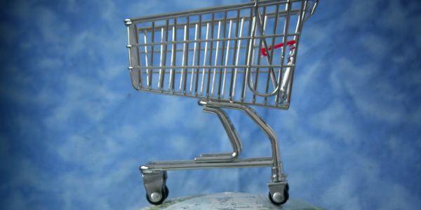 Miniature shopping cart on a globe against a blue sky background.