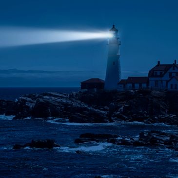 Lighthouse beam cutting through the night over rocky coast.