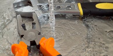 Two pliers are submerged in flowing water, one with orange handles and the other with black and yellow handles.